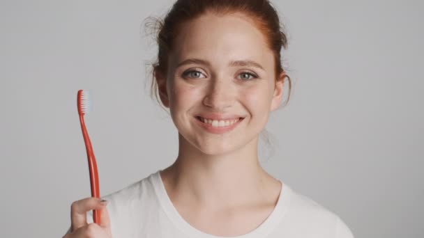 Крупним планом весела дівчина тримає зубну щітку щасливо дивлячись в камеру на білому тлі. Щасливий вираз
 - Кадри, відео