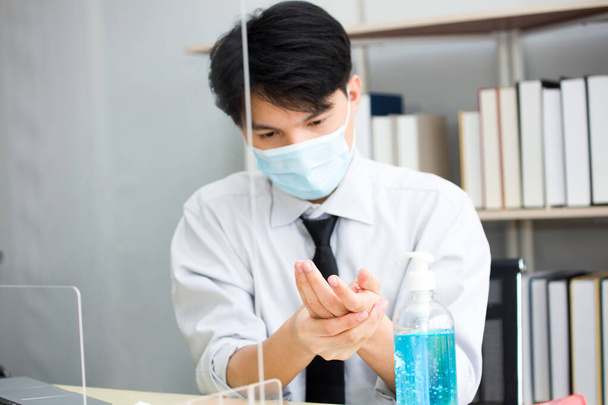 Los empleados masculinos asiáticos trabajaron en oficinas durante el brote del coronavirus (COVID-19), lleva una máscara facial higiénica y se lava regularmente las manos con gel de alcohol para protegerse.. - Foto, Imagen