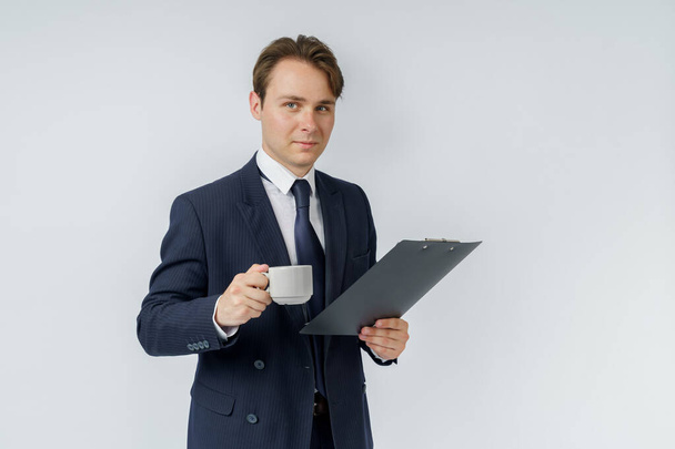 Businessman holds a cup of coffee and a tablet in his hands. White background. Business and finance concept - Фото, изображение