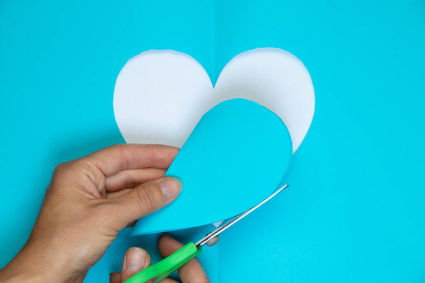 бумага голубое сердце и рука с ножницами вырезаны на цветном фоне близко - Фото, изображение