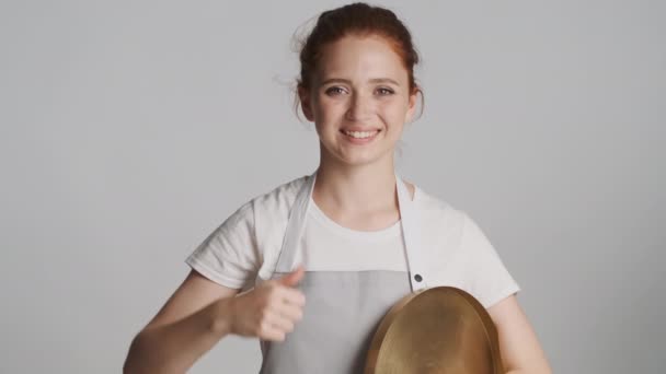 Belle serveuse souriante dans un tablier avec plateau montrant joyeusement le pouce levé et des gestes corrects à la caméra sur fond blanc - Séquence, vidéo