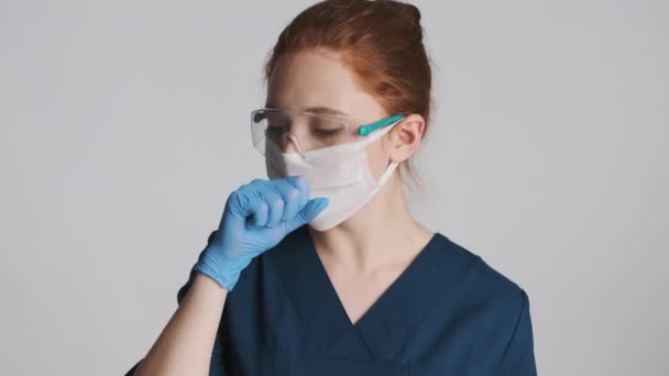 Female doctor in protective eyeglasses, mask and medical gloves coughing over white background. Feeling bad expression - Felvétel, videó