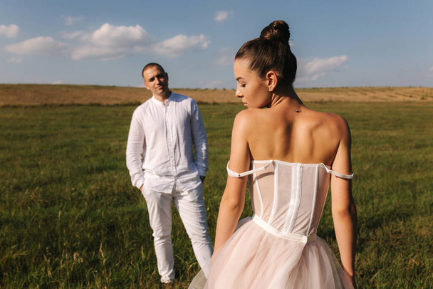 Gorgeous bride with handsome groom walkin in the field after wedding ceremony. Newlyweds posing to photographer - Φωτογραφία, εικόνα