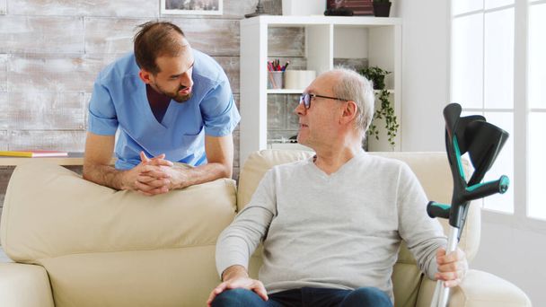 Пожилой мужчина беседует с медсестрой-мужчиной в уютном доме престарелых - Фото, изображение
