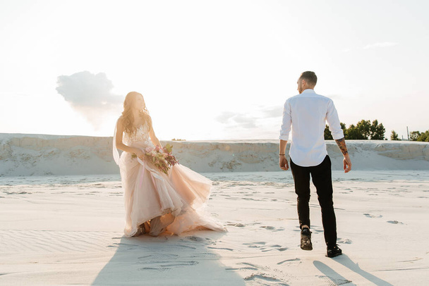 Love Story of a beautiful couple in a pink wedding luxury dress with a bouquet in the Sahara desert, sand, dunes - Foto, afbeelding