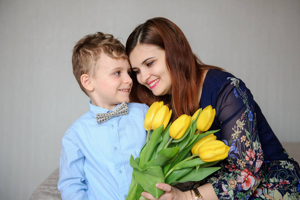 close-up foto van een jongen met gele tulpen in zijn hand knuffelen zijn gelukkig moeder - Foto, afbeelding