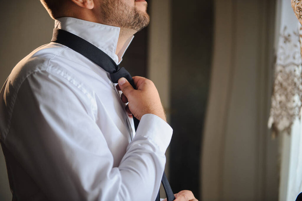 lateral view of a groom in white shirt that arranges his black tie - Fotografie, Obrázek