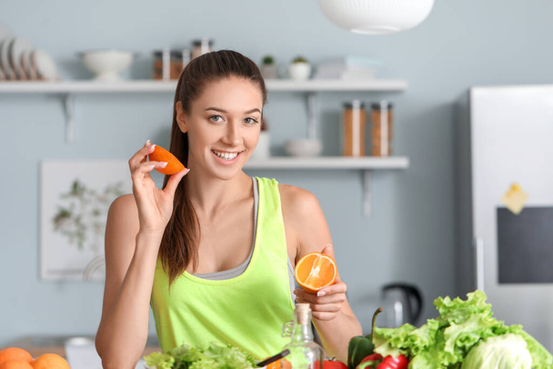 Beautiful young woman with fresh orange fruit in kitchen - Photo, Image