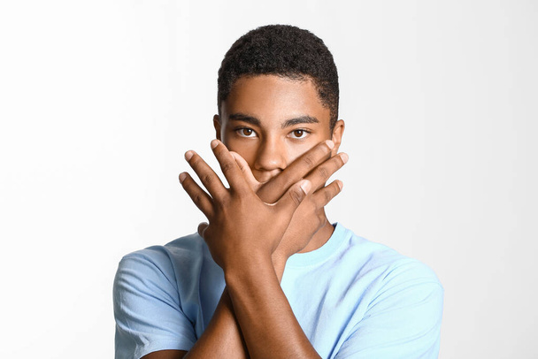 Een trieste Afro-Amerikaanse tiener die zijn mond bedekt met een lichte achtergrond. Stop racisme - Foto, afbeelding