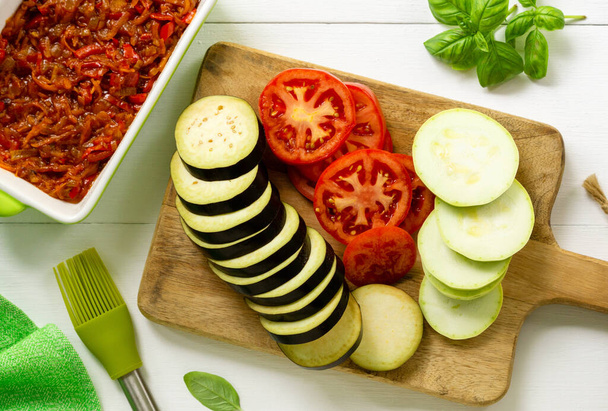 Ingredients for cooking ratatouille. Slices of eggplant, tomato and zucchini on a wooden cutting board - 写真・画像