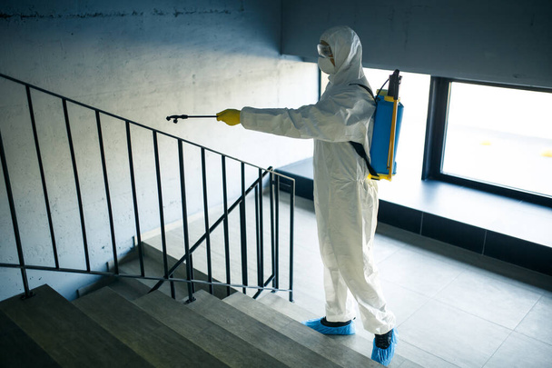 Puhdistus työntekijä siivoamassa portaikko ostoskeskuksessa antiseptistä estää covid-19 leviämistä. Mies desinfiointipuvussa suihkuttaa portaita. Terveydenhuollon, karanteenin ja hygienian käsite - Valokuva, kuva