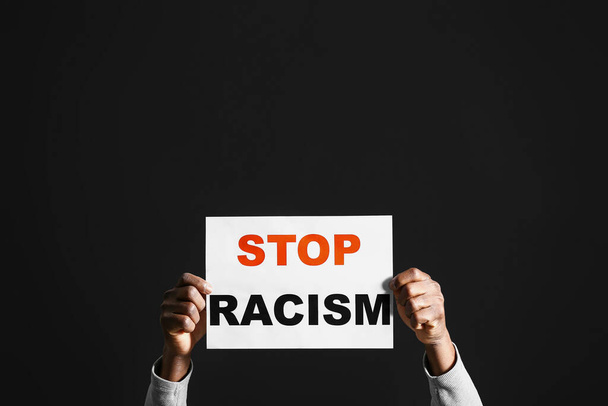 Homme afro-américain avec affiche sur fond sombre. Arrêtez le racisme - Photo, image