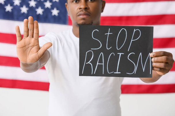 Грустный афроамериканец с плакатом, показывающим жест остановки возле национального флага США. Остановить расизм - Фото, изображение
