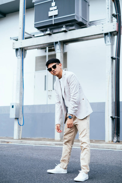 Un hombre de traje blanco con gafas de sol de pie como un jorobado al lado de la fábrica
. - Foto, Imagen