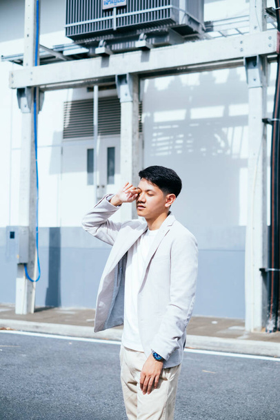 A man in white suit rubbing his eye while standing in the sunlight. - 写真・画像