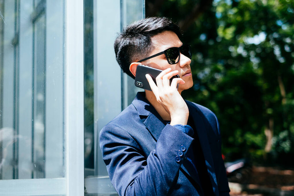 Koyu mavi takım elbiseli genç adam gözlük binasında telefonla konuşuyor.. - Fotoğraf, Görsel