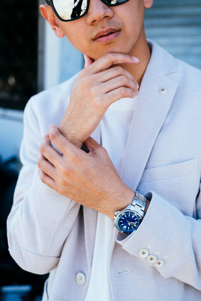A man in white suit and sunglasses standing and touch his wrist and chin like a model. - Фото, изображение