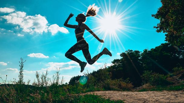 Silhouette eines Mädchens, das in den Bergen vor blauem Himmel und hartem Sonnenlicht springt. Sport im Freien zu treiben. Yoga praktizieren. - Foto, Bild