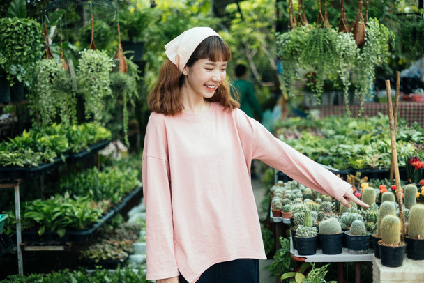 Bruneta dívka v béžové čelence a růžový dlouhý rukáv tričko stojící ve skleníku a namířit její index na dítě kaktus. - Fotografie, Obrázek