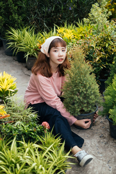 Tuinier meisje omarmen een dennenboom pot met liefde op de loopbrug van een tuin. - Foto, afbeelding