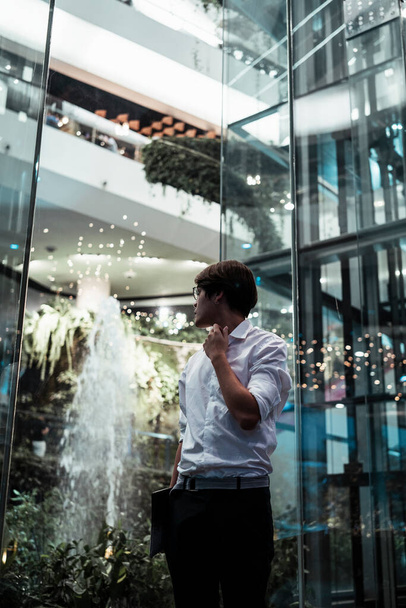 Black hair guy in semi-formal clothes standing in front of glasses elevator next to the fountain in the shopping mall. - Foto, Bild