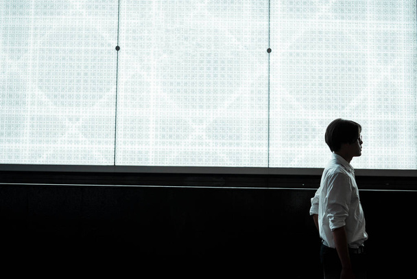 Plan de la silhouette du gars en chemise blanche debout avec son téléphone portable devant le panneau publicitaire du centre commercial avec lumière blanche. - Photo, image