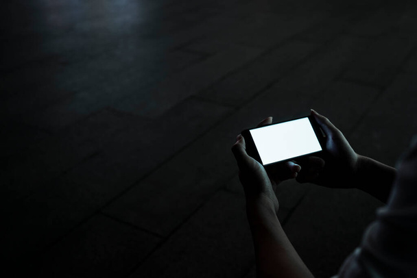 Cropped image of smartphone with the light on display while the man use it for game and social media in the city at night. - Zdjęcie, obraz