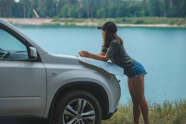 vrouw controleren met kaart op de SUV auto kap meer met blauw water op de achtergrond kopieerruimte - Foto, afbeelding