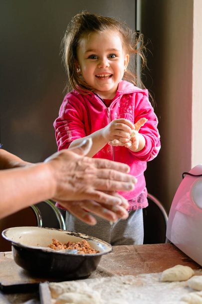 A casa, nipote e nonna cucinano gnocchi in cucina. nachika da carne, la nipote è felice che sua nonna insegni. - Foto, immagini