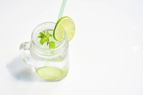 Стакан лимонада с зеленым ломтиком лимона и мятным листом, мед изолированный на белом фоне, летний напиток, свежий, напиток, домашний, прохладный, фруктовый сок, вид сбоку - Фото, изображение