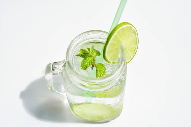 Mason βάζο ποτήρι λεμονάδα με πράσινη φέτα λεμονιού και φύλλα δυόσμου, μέλι που απομονώνονται σε λευκό φόντο, καλοκαιρινό ποτό, φρέσκο, ποτό, σπιτικό, δροσερό, χυμό φρούτων, πλαϊνή άποψη - Φωτογραφία, εικόνα