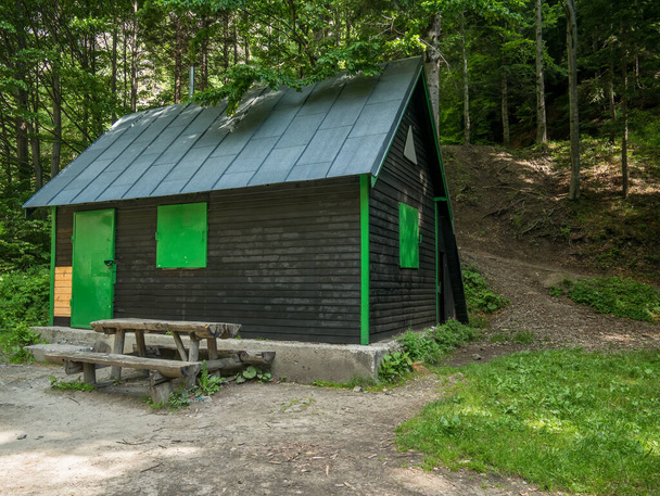 Kleines Haus mit Holztisch und Bank im Wald. Berghütte in den Bucegi-Bergen. - Foto, Bild