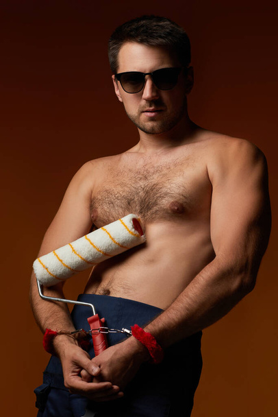 sexy caucasian man worker handcuffed holding paint roll - Фото, изображение