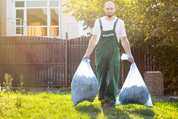 Bahçıvan gübre torbalarını çıkarır. Açık yeşil üniforma.. - Fotoğraf, Görsel