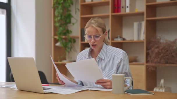 An angry nervous young blonde businesswoman is screaming and throwing out her paper documents sitting in the office - Materiaali, video
