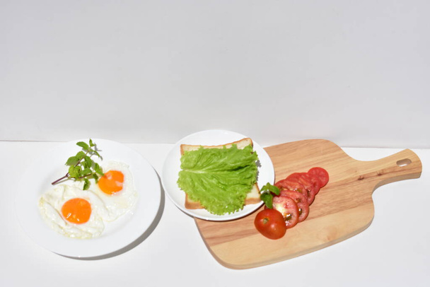 Healthy breakfast meal with sandwiches, fried eggs, tomato slice, salad, mint leaves, wooden cutting board, white background, sunny, junk food, lose weight, organic, simplicity, vegan, burger, low fat, fitness meal, close up - Foto, imagen
