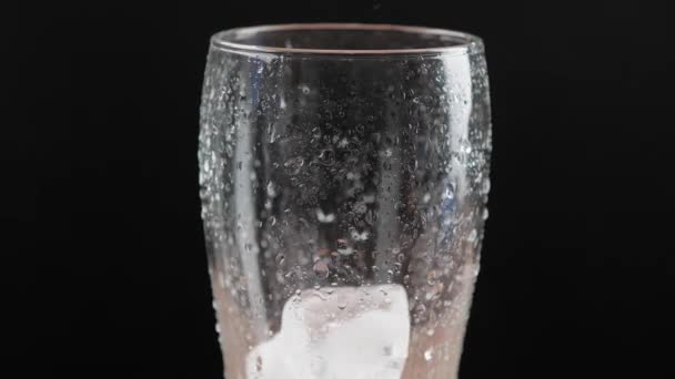 Het laten vallen van ijsblokjes in glas op donkere achtergrond, close-up - Video