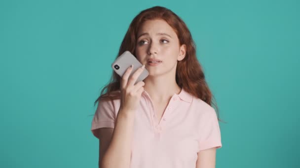 Attraente casual rossa ragazza registrazione messaggio vocale su smartphone sognante guardarsi intorno su sfondo colorato - Filmati, video
