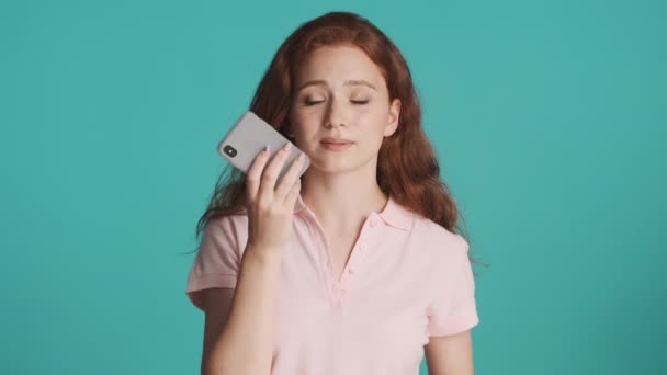 Bella ragazza rossa sorridente che registra felicemente il messaggio vocale sullo smartphone su sfondo colorato - Filmati, video