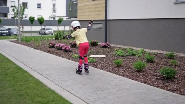 A little girl is rollerblading in the courtyard of an apartment building. The child is just beginning to master roller skates, so he often falls. - Filmati, video