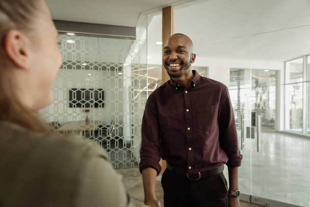 Lachende jonge Afrikaanse zakenman praten met een collega werk terwijl ze samen in een modern kantoor - Foto, afbeelding