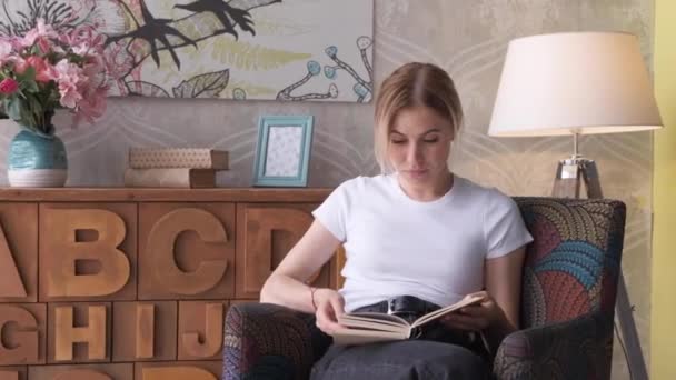 Young woman reading book in cozy living room, turning page, learning, studying, education, read books, stay home concept - Imágenes, Vídeo