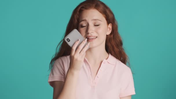 Beautiful redhead girl tiredly recording voice message on smartphone over colorful background - Filmagem, Vídeo