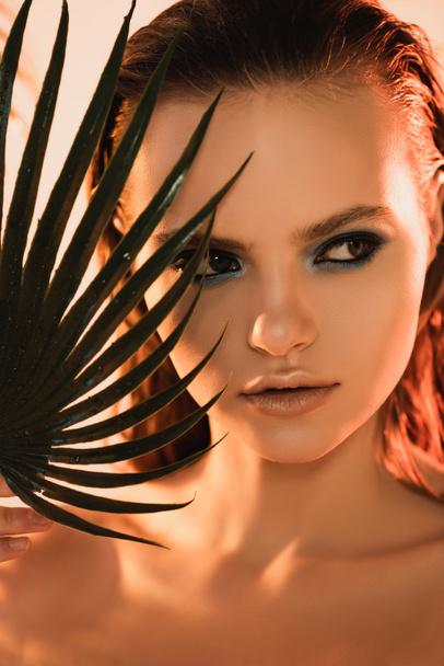 close up of beautiful woman with makeup looking away near palm leaf - Foto, imagen