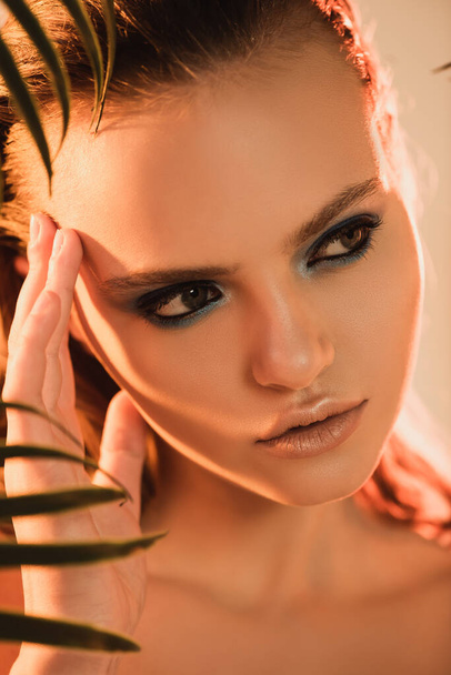 selective focus of beautiful woman with makeup looking away near palm leaf - Photo, Image