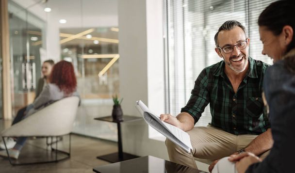 Usmívající se zralý podnikatel procházející papírování s kolegou, zatímco sedí spolu v salonku prostoru moderní kanceláře - Fotografie, Obrázek
