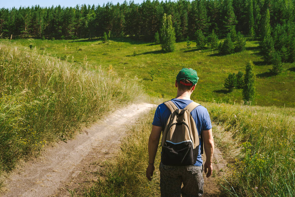Młody turysta z plecakiem i czapką spaceruje po alpejskich łąkach i górach. - Zdjęcie, obraz