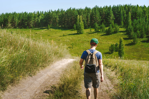 Egy fiatal turista hátizsákkal és sapkával sétál az alpesi rétek és hegyek között. - Fotó, kép