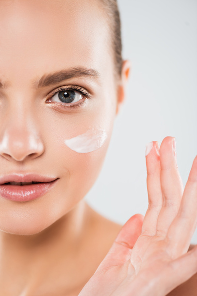 vista cortada de jovem mulher aplicando creme facial isolado no cinza
  - Foto, Imagem