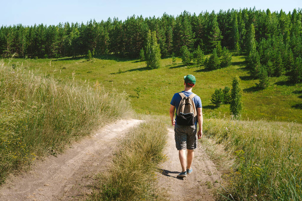 Mladý muž turista s batohem a čepicí prochází alpskými loukami a horami - Fotografie, Obrázek